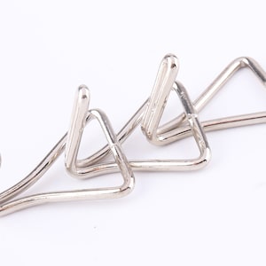 May include: Three silver metal hooks with a triangular shape. The hooks are designed to hang items on a wall or other surface.