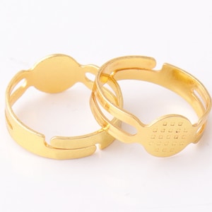 Op de afbeelding: Twee ringblanken van goudkleurig metaal met ronde bezels. Eén bezel heeft een glad oppervlak, de andere een getextureerd oppervlak.
