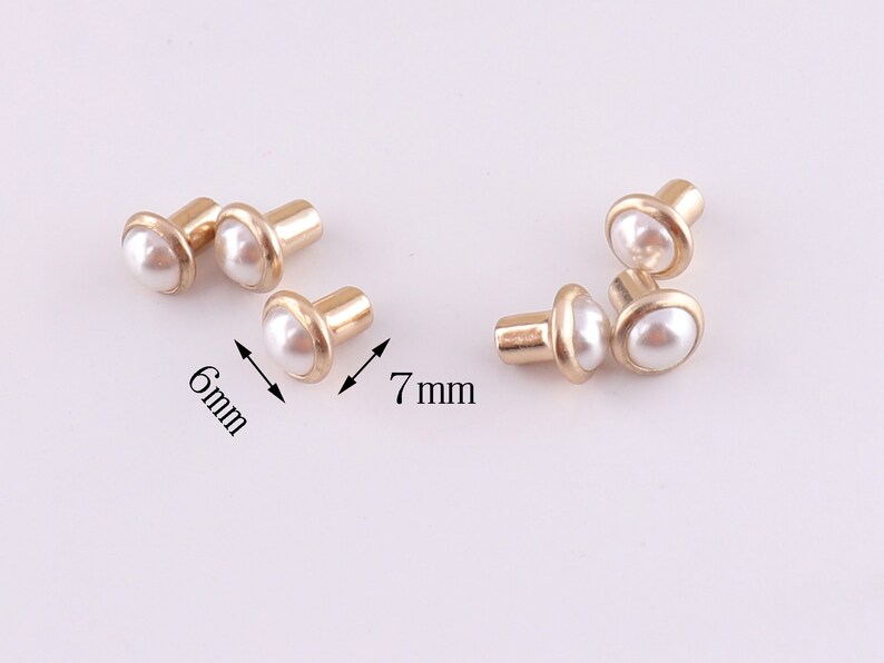 Puede incluir: Seis tachuelas de metal dorado con tapas de perla blanca. Las tachuelas tienen un di&aacute;metro de 6 mm y 7 mm.
