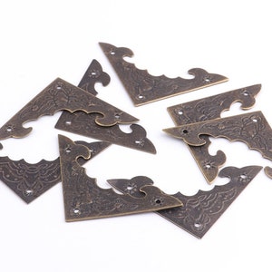 Peut inclure: Un ensemble de huit coins de renfort en or antique avec des motifs floraux complexes. Les coins de renfort sont en métal et ont une finition vieillie.