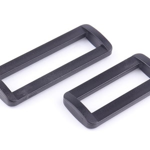 May include: Two black plastic slider buckles. The buckles are rectangular with a slot in the centre. They are commonly used for straps, bags, and other accessories.