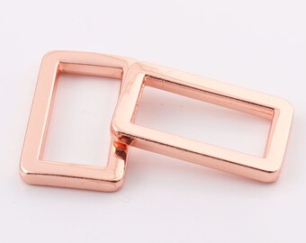Puede incluir: Dos hebillas deslizantes rectangulares de metal color oro rosa. Las hebillas están apiladas una encima de la otra.