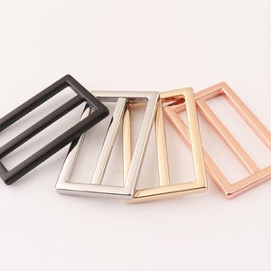 Puede incluir: Cuatro hebillas deslizantes de metal en diferentes acabados: negro, plateado, dorado y oro rosa. Cada hebilla tiene una forma rectangular con dos líneas paralelas en el centro.