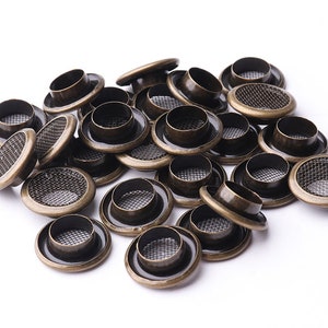 May include: A pile of antique brass eyelets with a mesh centre. The eyelets are round and have a raised edge.