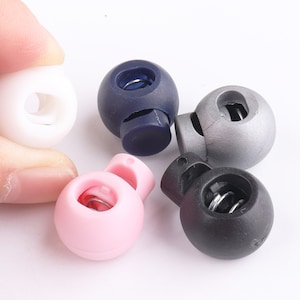 May include: Five plastic toggle clasps in different colors: white, navy blue, silver, pink, and black. Each clasp has a spring mechanism and a hole for threading cord or string.