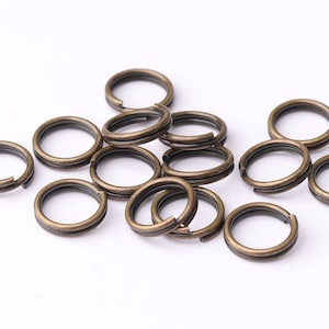 May include: A group of 14 antique gold-toned jump rings. The jump rings are all the same size and are arranged in a pile.