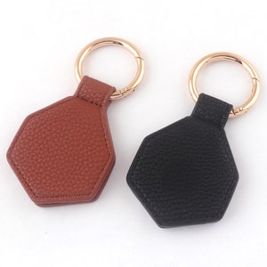 May include: Two leather keychains with hexagon-shaped tags. One keychain is brown and the other is black.