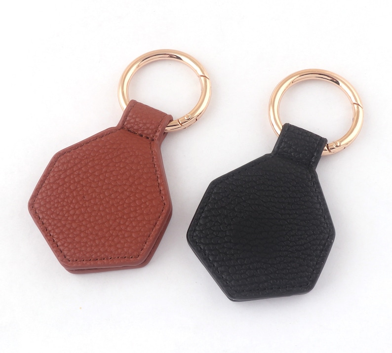 May include: Two leather keychains with hexagon-shaped tags. One keychain is brown and the other is black.