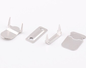 May include: Four silver metal garment fasteners, two are rectangular with a hole in the center, and two are shaped like a hook with a rounded end.