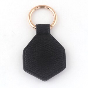 May include: A black leather hexagon-shaped keychain with a rose gold metal ring.