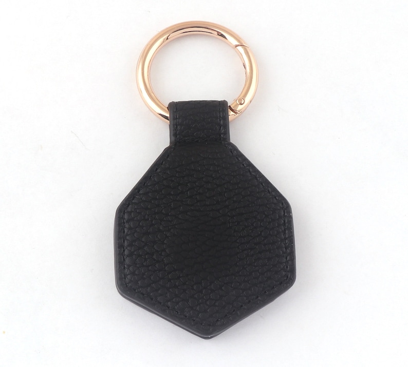 May include: A black leather hexagon-shaped keychain with a rose gold metal ring.