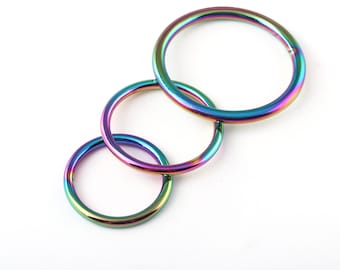 May include: Three iridescent metal rings of different sizes, stacked on top of each other. The rings are a rainbow of colors, including purple, blue, green, and red.