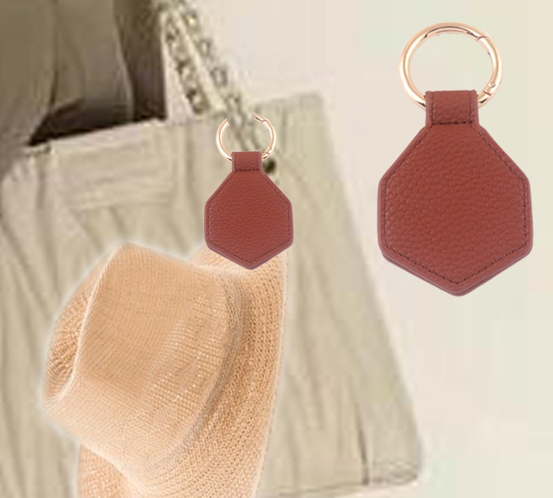 May include: A brown leather hexagon-shaped keychain with a gold ring. The keychain is attached to a white bag.