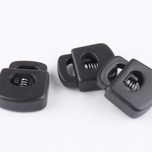 May include: Four black plastic clasps with a spring mechanism. The clasps are designed to be used for securing straps or cords.
