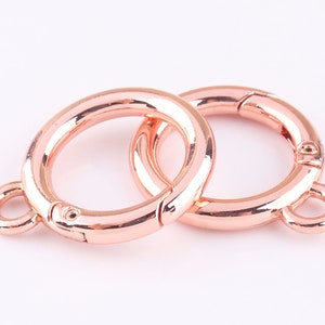 May include: Two rose gold metal key rings with a swivel clasp. The key rings are connected to each other.