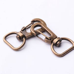May include: Two antique gold-toned metal swivel clasps with a D-ring on each end.