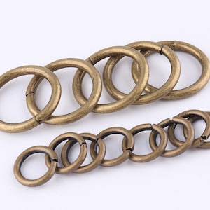 Könnte beinhalten: Ein Satz mit 12 antiken goldfarbenen Metall-Sprühringen. Die Sprüringe sind in zwei Größen, mit sechs größeren Ringen und sechs kleineren Ringen.