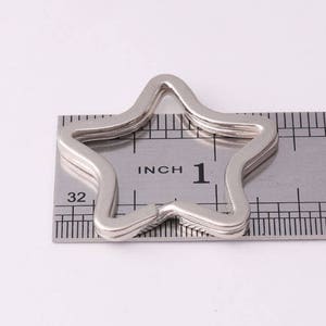 May include: A silver star-shaped key chain ring measuring 1 inch in diameter, shown next to a ruler.
