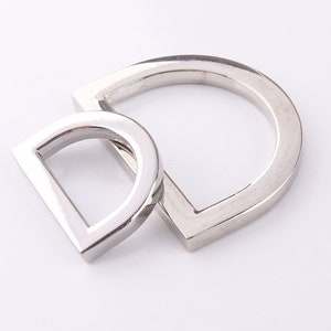 May include: Two silver metal D-rings, one larger than the other, are shown on a white background. The rings are smooth and shiny.