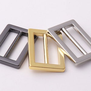 May include: Three metal belt buckle slides in different finishes: black, gold, and silver.