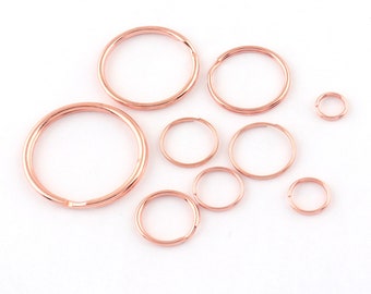 Op de afbeelding: Een set van negen roségouden sleutelringen in verschillende maten. De sleutelringen zijn gemaakt van metaal en hebben een gladde, gepolijste afwerking.