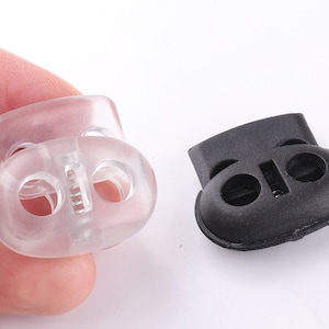 May include: Two toggle cord locks, one clear plastic and one black plastic. Both have two holes for cord ends.