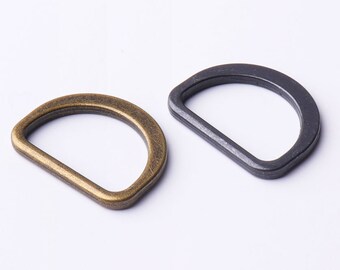 May include: Two metal D-rings, one in antique brass and one in black, are shown on a white background. The rings are about 1 inch in diameter.