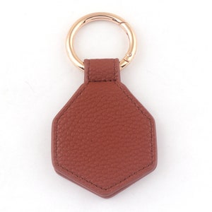 May include: A brown leather hexagon-shaped keychain with a gold metal ring.