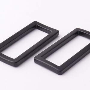 May include: Two black metal rectangular slider buckles. The buckles are about 2 inches long and 1 inch wide.