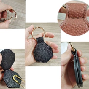 May include: A black leather key chain with a hexagonal shape. The keychain has a gold metal ring and opens to reveal a small pocket inside.