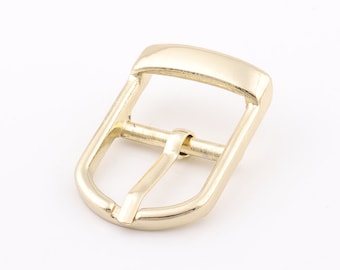 May include: A gold-toned metal buckle with a smooth, rounded finish. The buckle is designed for a belt or strap.