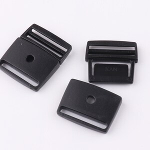 May include: Three black plastic buckles with a single hole and a slot for a strap. The buckle on the right has the word "KAM" printed on it.