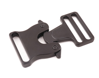 May include: A black metal buckle with a hinged design. The buckle has two rectangular sections with slots for webbing and a pivoting mechanism for secure closure. The hardware is shown against a white background.