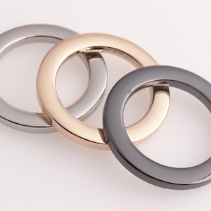 May include: Three metal rings in different finishes: silver, gold, and black. The rings are interlocked, creating a decorative design.