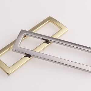 Puede incluir: Dos tiradores de cajón rectangulares de metal, uno dorado y otro plateado, con un borde biselado.