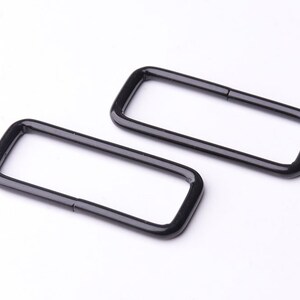 May include: Two black metal D-rings, each with a rectangular shape and a smooth, polished finish.