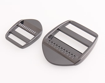 May include: Two black metal slider buckles. The larger buckle is about 4.5 inches long and 2 inches wide. The smaller buckle is about 2.5 inches long and 1.5 inches wide.