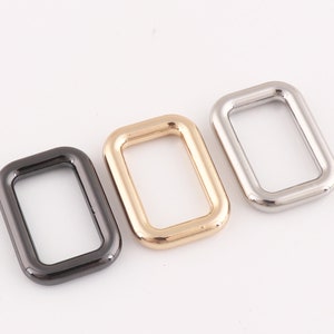 Puede incluir: Tres anillos rectangulares de metal en diferentes acabados: negro, dorado y plateado. Los anillos miden aproximadamente 5 cm de largo y 2,5 cm de ancho.