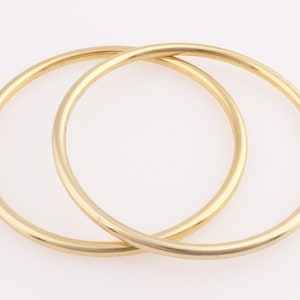 Op de afbeelding: Twee gouden armbandjes, waarvan er &eacute;&eacute;n iets groter is dan de andere, liggen op elkaar.