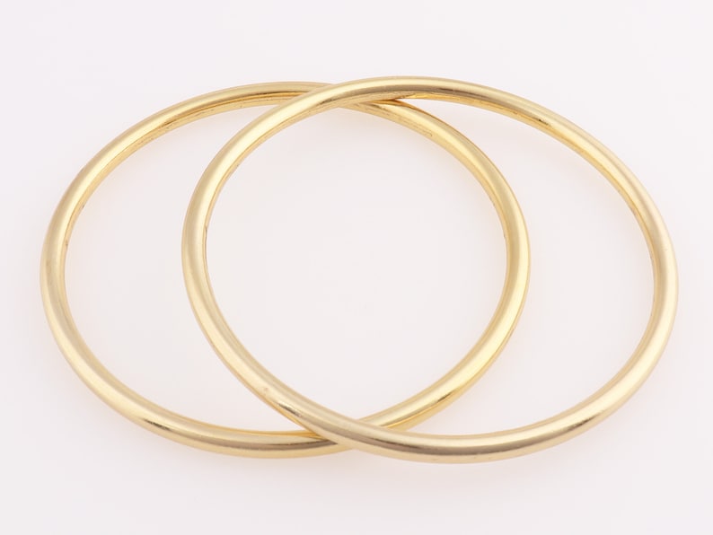 Op de afbeelding: Twee gouden armbandjes, waarvan er &eacute;&eacute;n iets groter is dan de andere, liggen op elkaar.