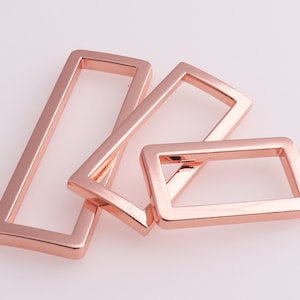 May include: Four rose gold metal rectangular rings of different sizes.