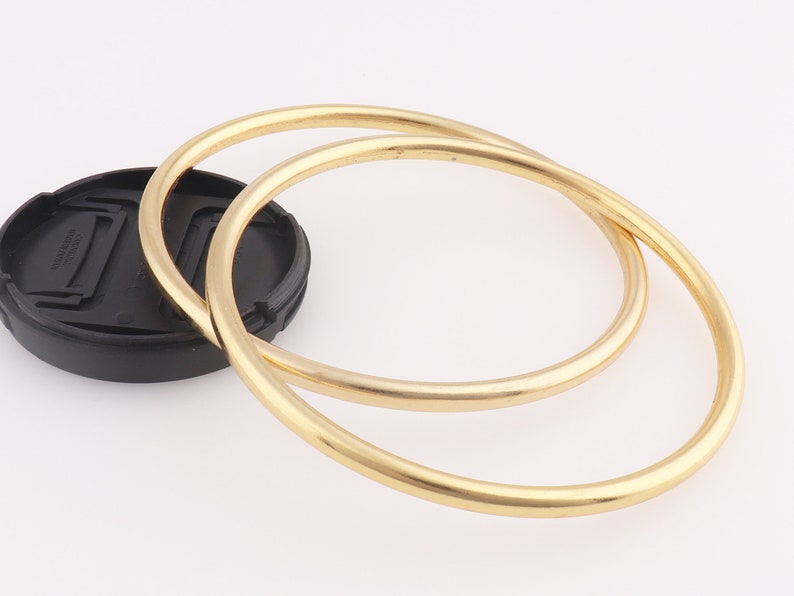 Op de afbeelding: Twee gouden metalen armbanden, waarvan er &eacute;&eacute;n iets groter is dan de andere, liggen op elkaar.