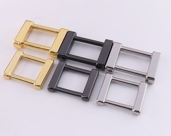 May include: Four metal belt buckle loops in gold, black, and silver. The loops are rectangular with a square opening in the center.