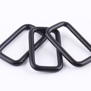 Könnte beinhalten: Drei schwarze D-Ringe aus Metall, jeweils mit rechteckiger Form und glatter Oberfläche.