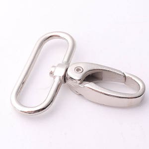 Op de afbeelding: Zilveren metalen draaihaak met een D-ring. De haak is gesloten en de D-ring is open.