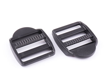 May include: Two black plastic slider buckles, each with three slots for webbing. The buckles are designed for securing straps or belts.