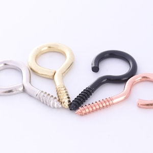 May include: Four screw-in hooks with different finishes: silver, gold, black, and copper. Each hook has a rounded eyelet and a threaded screw.