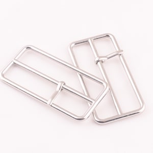 Puede incluir: Dos deslizadores de hebilla de cinturón de metal plateado. Los deslizadores son rectangulares con esquinas redondeadas y tienen un acabado liso y pulido.