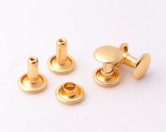 Può includere: Cinque rivetti in metallo color oro, alcuni con testa rotonda e altri con testa piatta. I rivetti sono utilizzati per fissare tessuto o pelle.