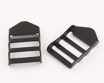 May include: Two black plastic strap buckles with three slots each. The buckles are designed to be used with straps or webbing.